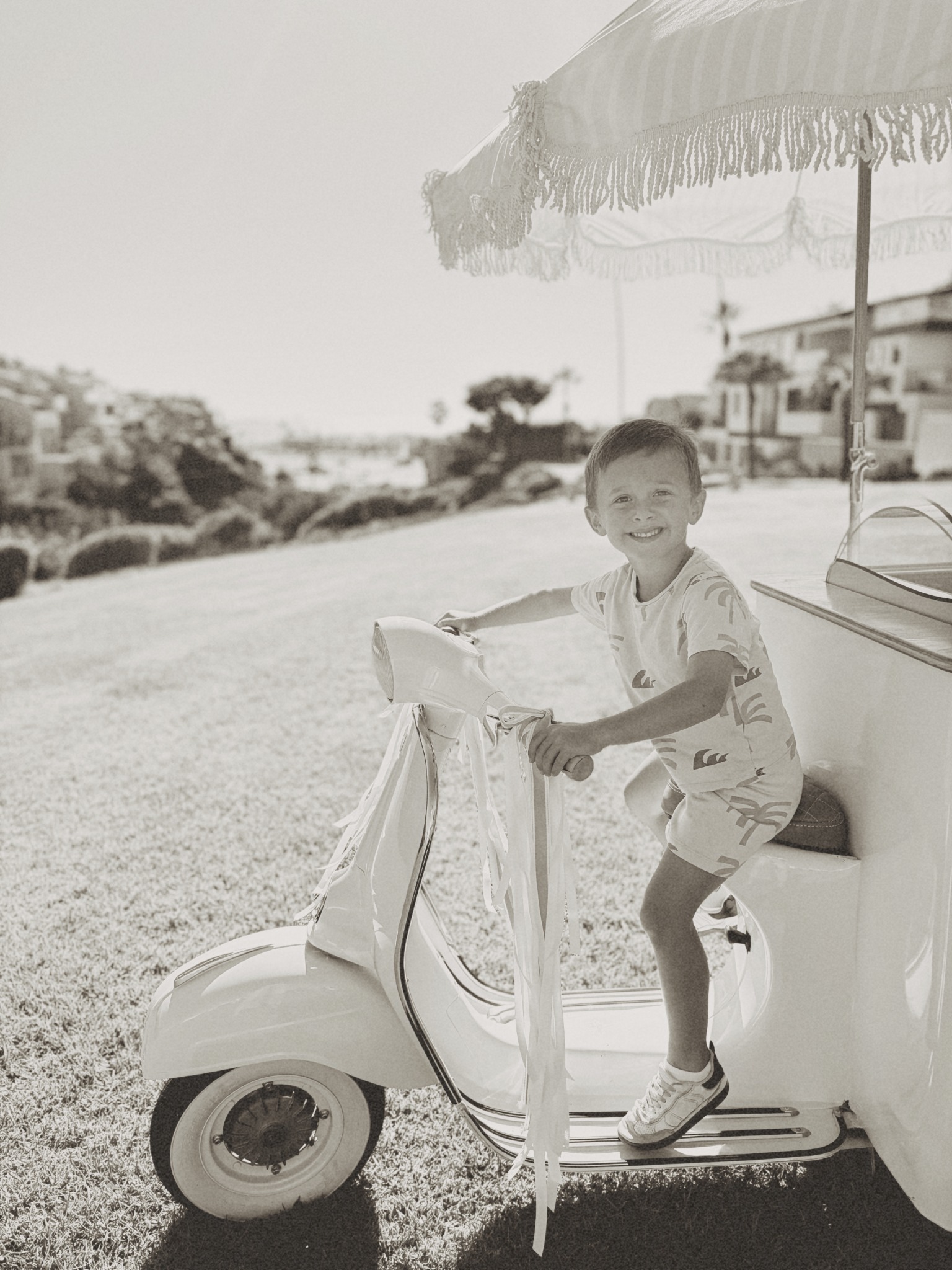 Black-and-white photograph of a smiling child sitting on the Fiorella Vespa