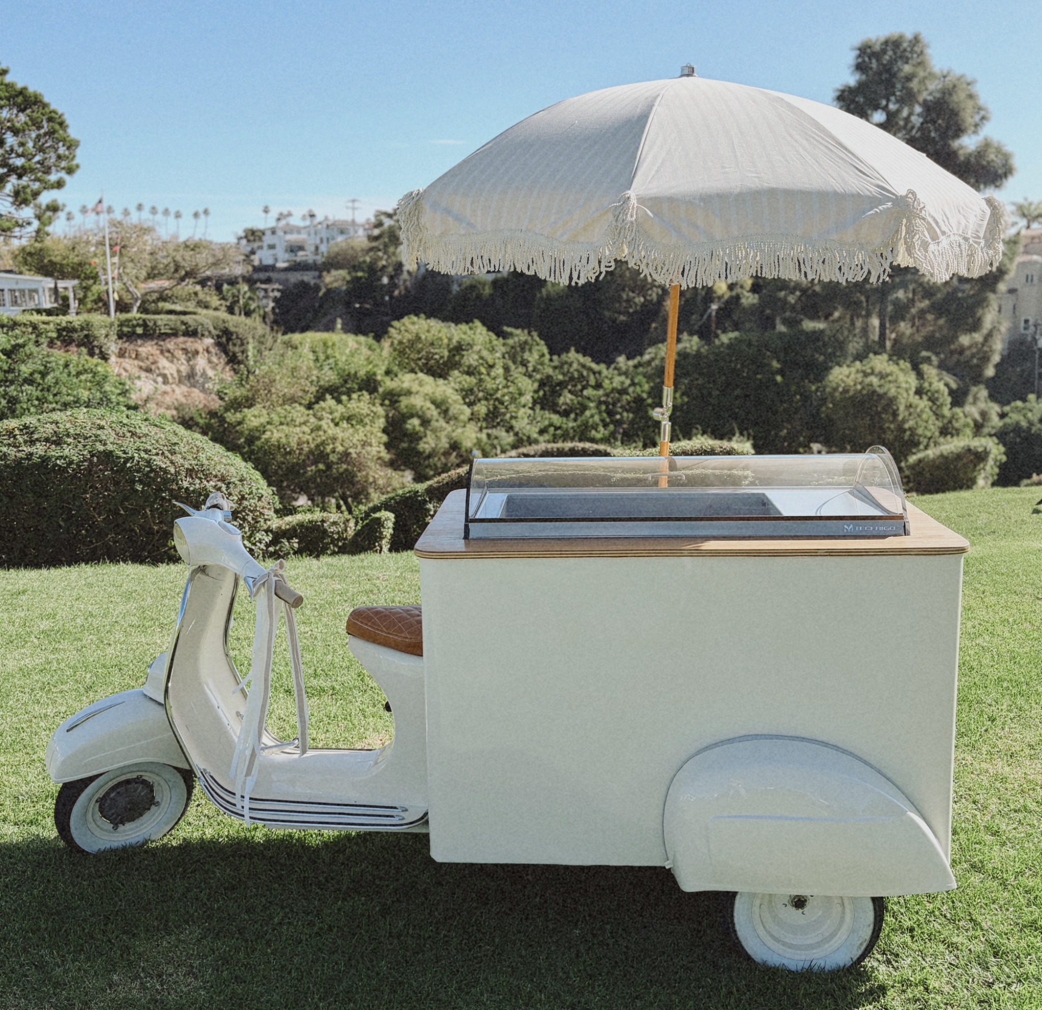 Full side view of Fiorella Vespa gelato bar and fringed umbrella on a lawn